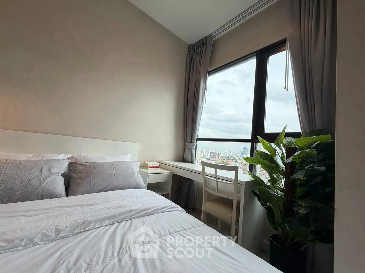 Modern bedroom with large window offering stunning city views, featuring cozy bed and stylish decor.