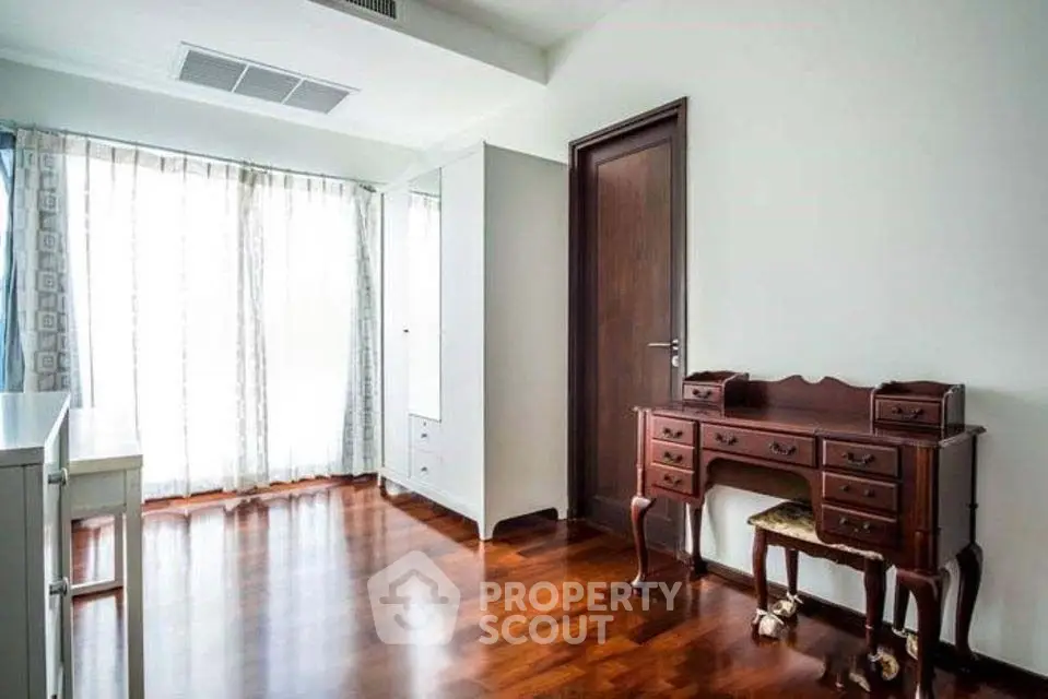 Spacious bedroom with elegant wooden flooring and classic furniture, featuring ample natural light through large windows.