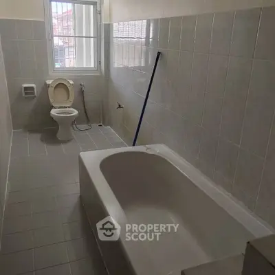 Spacious bathroom with bathtub and modern tiling, featuring natural light from large window.