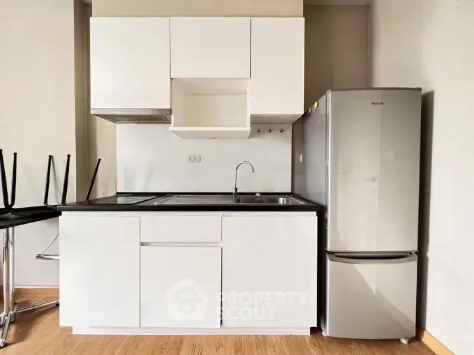 Modern compact kitchen with sleek white cabinets and stainless steel fridge.