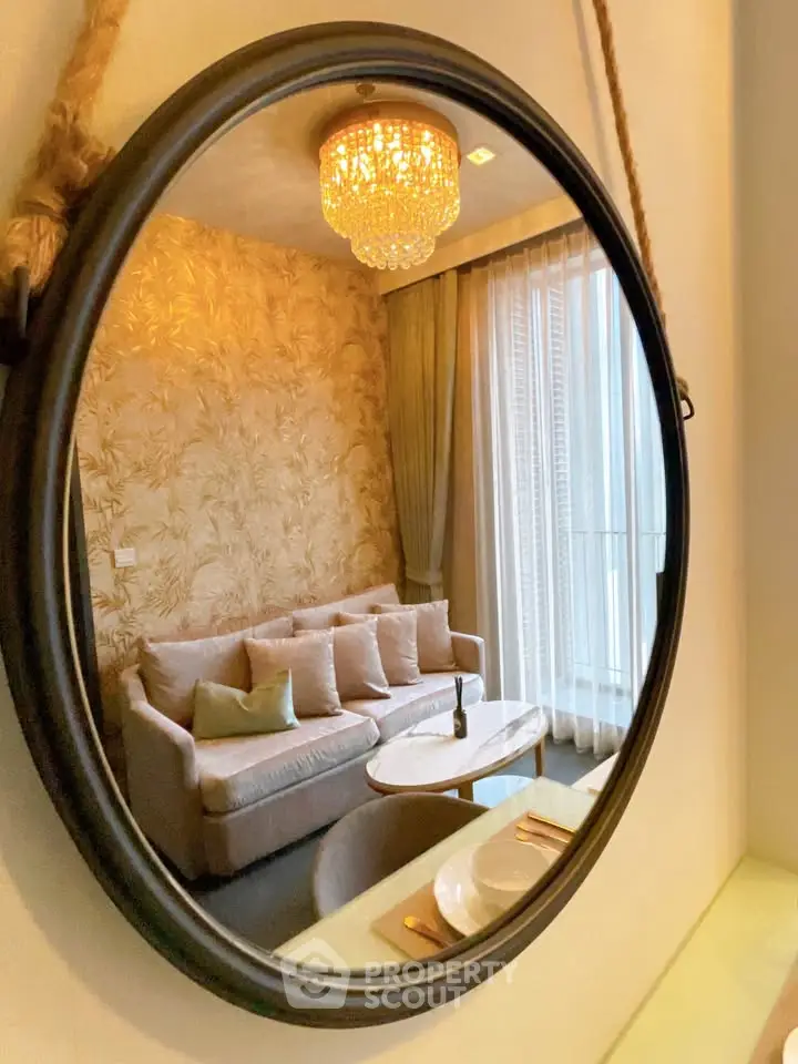 Elegant living room with chic decor and chandelier reflecting in a round mirror, showcasing luxury interior design.