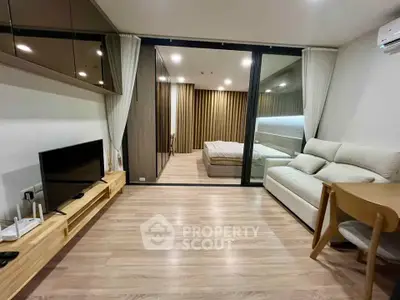 Modern open-plan living room with sleek furniture and a view into a cozy bedroom.
