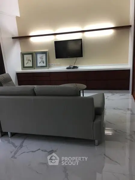 Modern living room with sleek furniture and marble flooring, featuring a mounted TV and elegant decor.