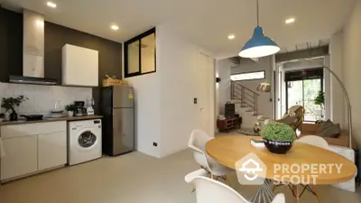 Modern open-plan living space with a sleek kitchen, dining area, and cozy lounge, featuring a washing machine and ample natural light.