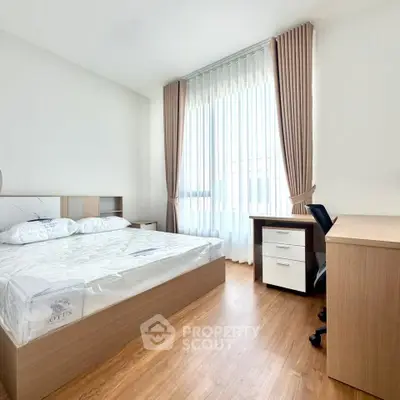 Bright and modern bedroom with wooden flooring and large window, perfect for a cozy living space.