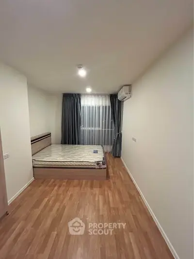 Spacious bedroom with wooden flooring and large window, perfect for comfort and relaxation.