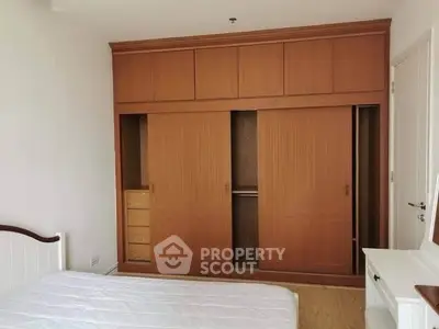 Spacious bedroom with built-in wooden wardrobe and cozy bed setup.