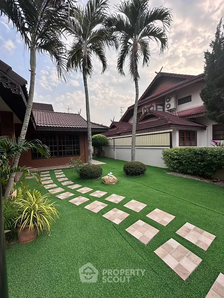 Charming suburban home with lush garden and palm trees, featuring a well-maintained pathway and traditional architecture.