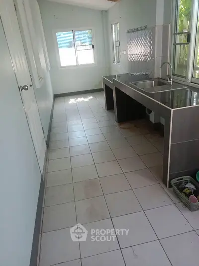 Spacious kitchen with dual sink and tiled flooring, ample natural light from large windows.