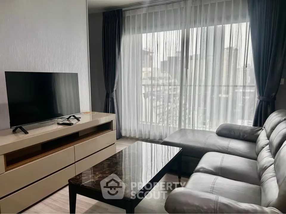 Modern living room with sleek furniture and large window offering city views.