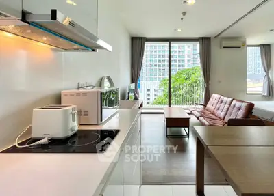 Modern open-plan living room with kitchen, featuring sleek appliances and a cozy seating area with city view.