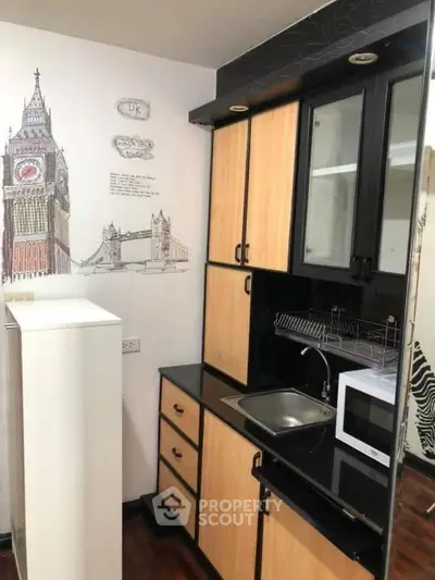 Compact kitchen with modern cabinets and microwave, featuring London-themed wall art.