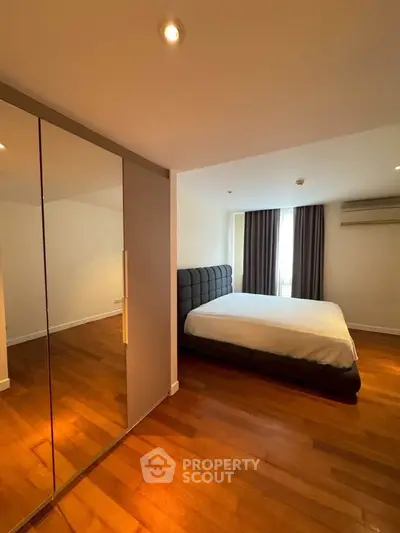 Spacious bedroom with wooden flooring and mirrored wardrobe in modern apartment.