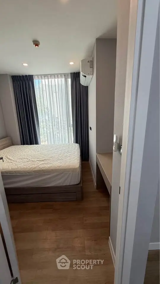 Modern bedroom with large window and wooden flooring, featuring a comfortable bed and air conditioning.