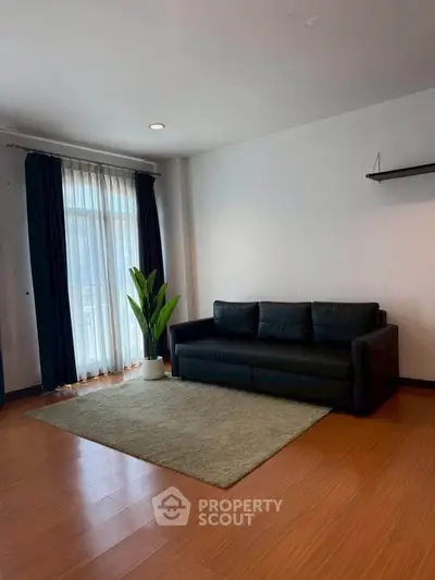 Spacious living room with sleek black sofa and large window for natural light.