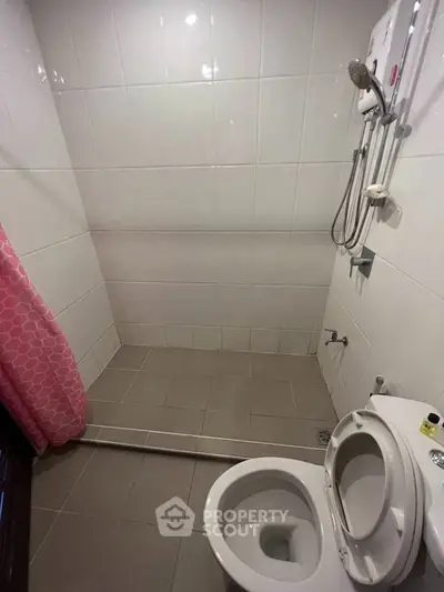 Compact bathroom with shower and toilet, featuring white tiles and a pink shower curtain.