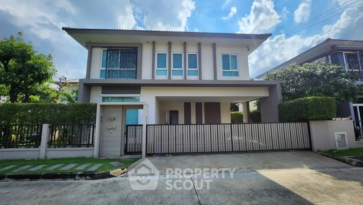 Modern two-story house with gated entrance and lush greenery