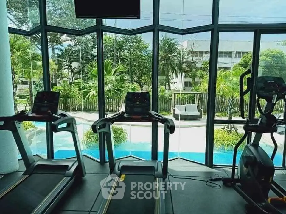 Modern gym with treadmills overlooking a scenic pool and lush greenery.