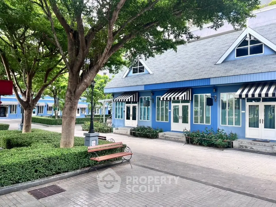 Charming blue building with striped awnings and lush greenery in a serene courtyard.