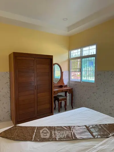 Cozy bedroom with wooden wardrobe and dressing table, featuring a large window for natural light.