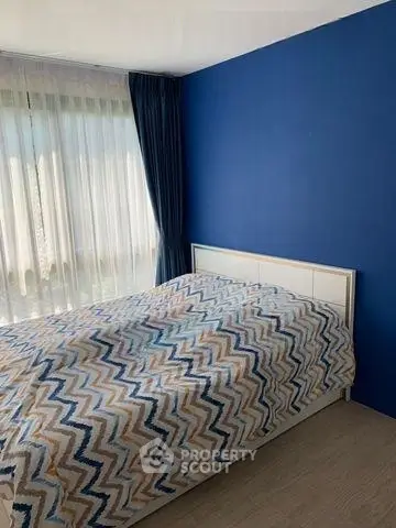 Cozy bedroom with modern blue accent wall and large window for natural light.