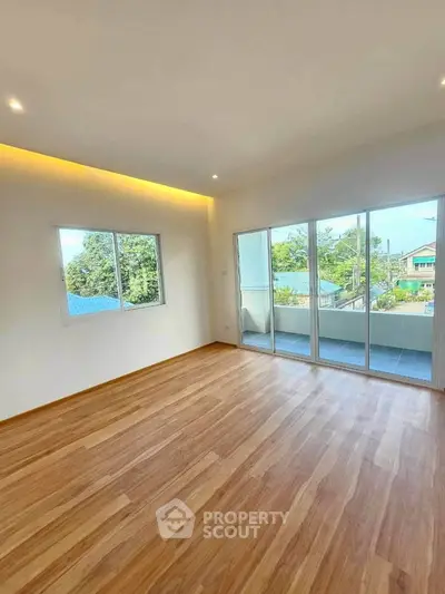 Spacious living room with large windows and balcony access, featuring elegant wood flooring and modern lighting.