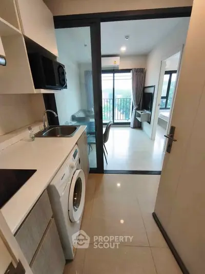 Modern apartment with open kitchen and living area, featuring a washing machine and balcony view.
