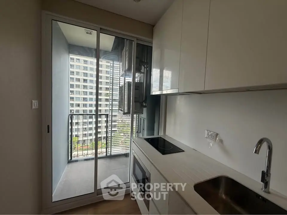 Modern kitchen with sleek white cabinets and glass door leading to a balcony with city view.