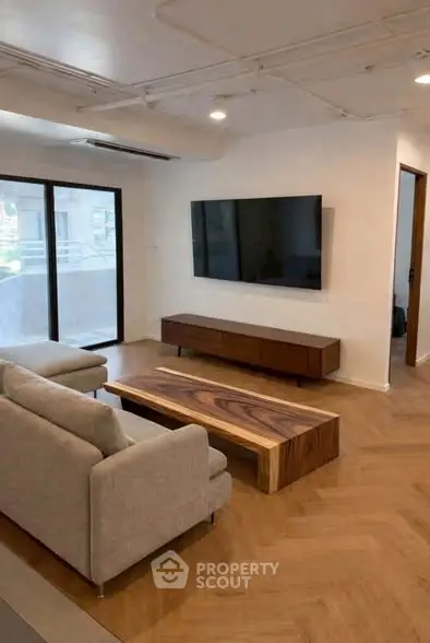 Modern living room with sleek furniture and large TV, featuring a stylish wooden coffee table and parquet flooring.