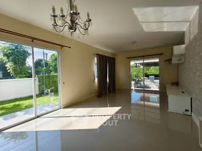 Spacious living room with chandelier and garden view, featuring large windows and elegant flooring.