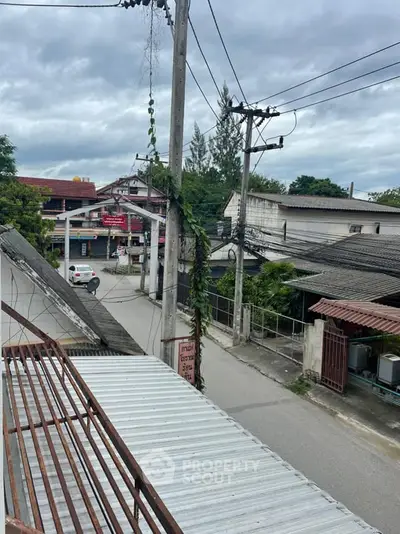 Street view from a balcony showcasing residential area with power lines and cloudy sky.