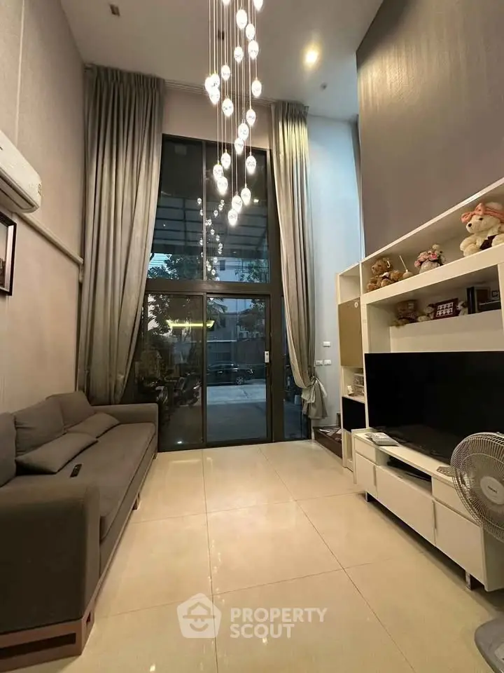 Spacious living room with high ceiling and modern decor, featuring a large window and elegant lighting.