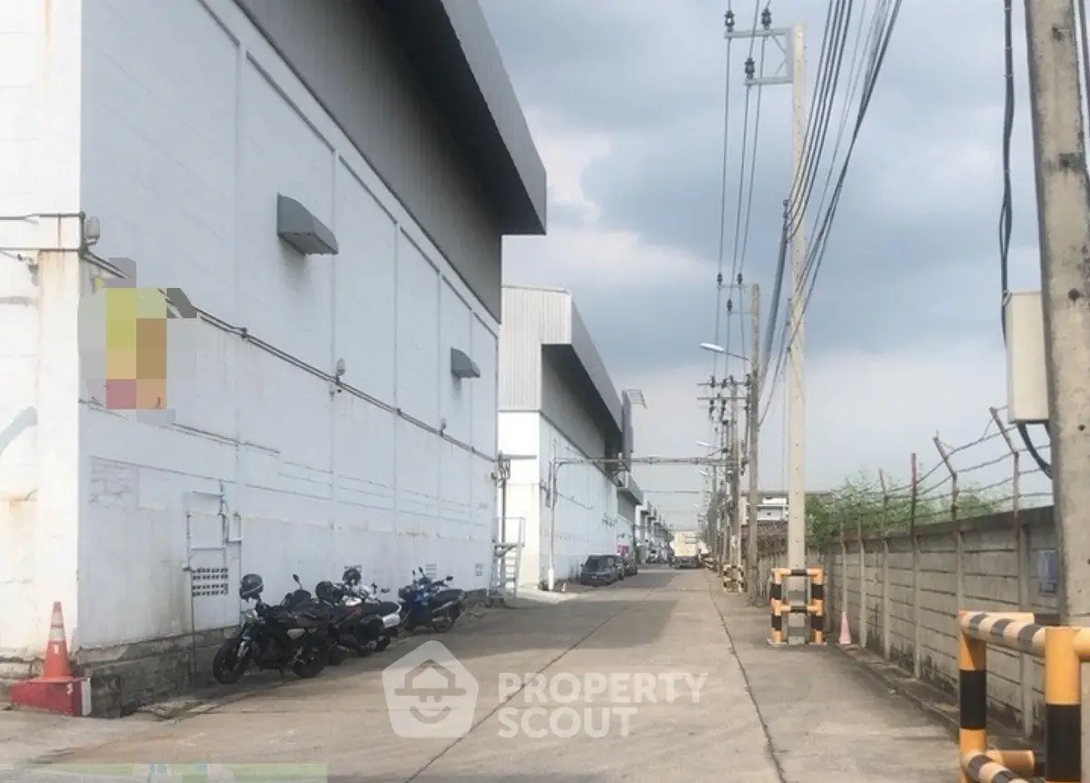Industrial warehouse exterior with parking and utility poles under cloudy sky.