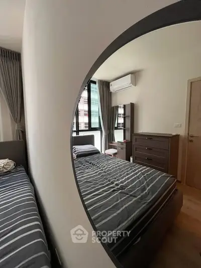 Modern bedroom with stylish decor, featuring a large mirror and ample natural light from windows.