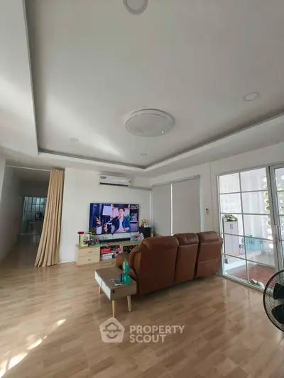 Spacious living room with modern decor and large TV, featuring natural light and wooden flooring.