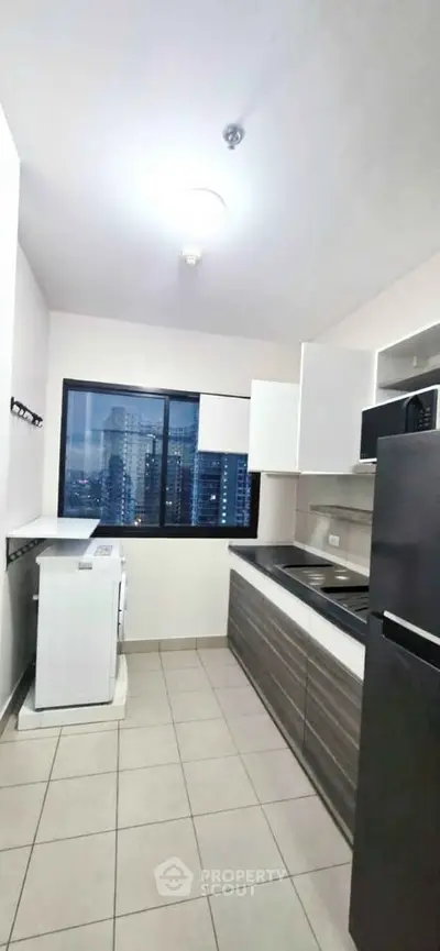 Modern kitchen with sleek cabinetry and city view from window, featuring a refrigerator and microwave.