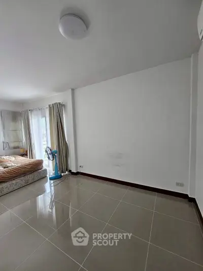Spacious bedroom with large windows and tiled flooring, offering ample natural light and modern design.