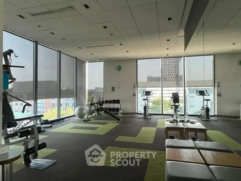 Spacious gym with modern equipment and large windows offering city views.