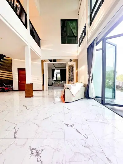 Luxurious open-plan living room with high ceilings and marble flooring, featuring large windows and elegant decor.