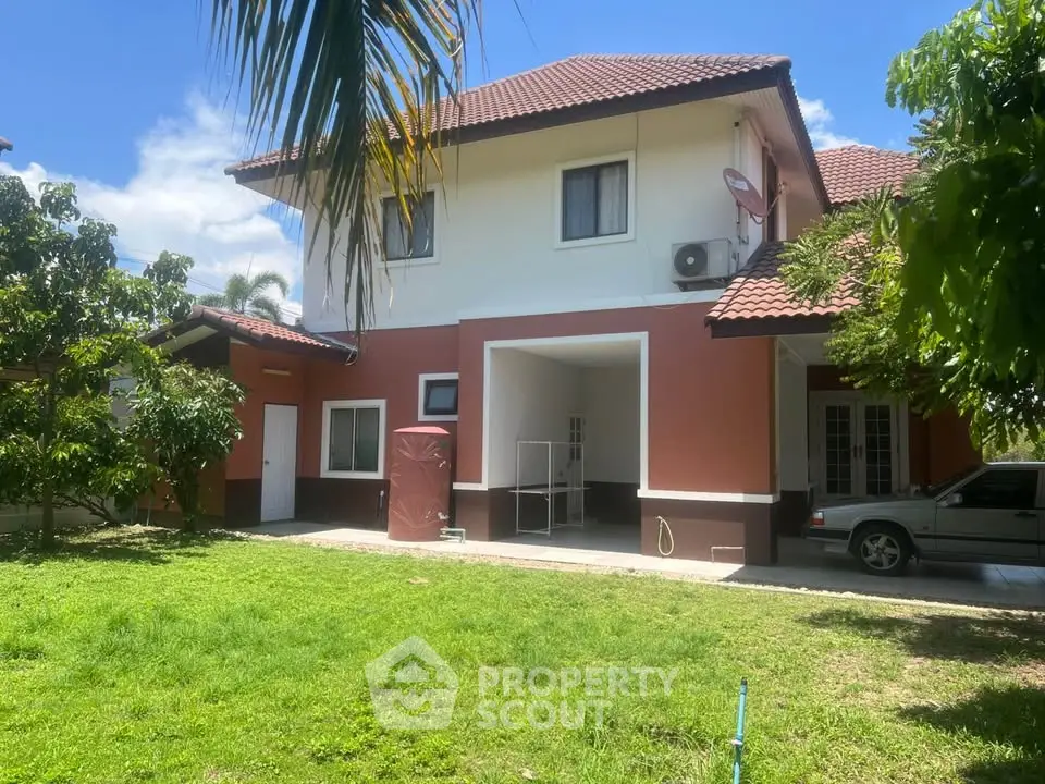 Charming two-story house with red-tiled roof and lush green garden, perfect for family living.