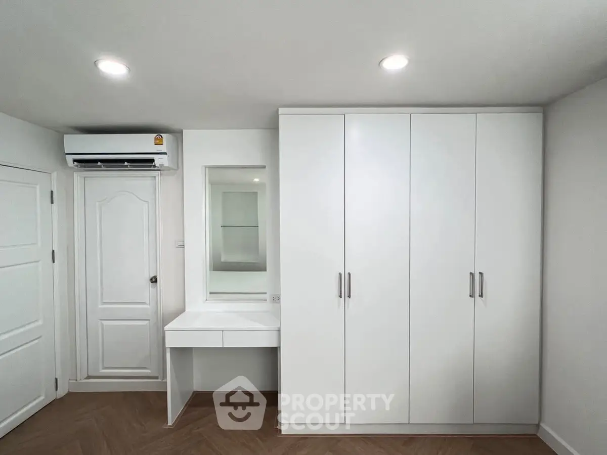 Modern bedroom with sleek white wardrobe and vanity, featuring recessed lighting and wood flooring.