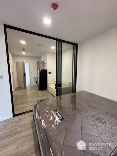 Modern apartment interior with bedroom and living area separated by glass doors, featuring sleek design and wood flooring.