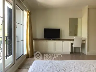 Spacious bedroom with large windows and elegant decor, featuring a TV and a cozy workspace.