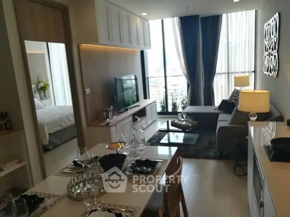 Modern open-plan living room with dining area and bedroom view, featuring elegant decor and natural light.