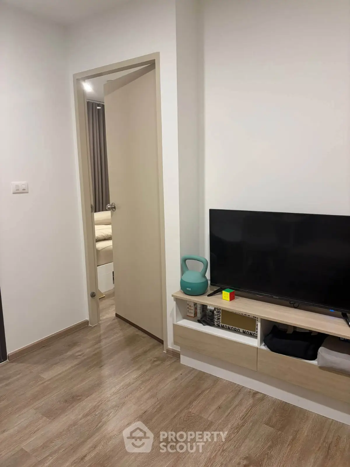 Modern living room with sleek TV stand and open doorway to cozy bedroom.