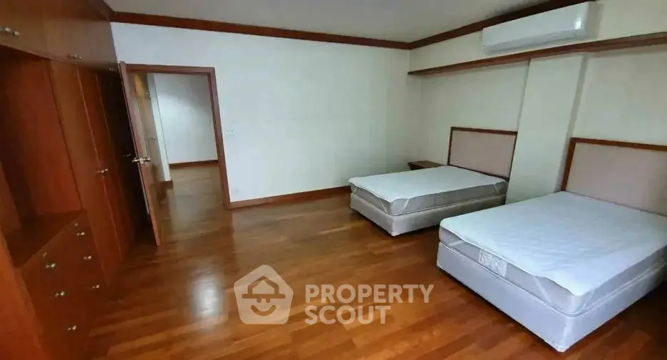 Spacious bedroom with twin beds and wooden flooring in modern apartment.