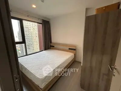 Modern bedroom with large window and city view, featuring a minimalist wooden bed frame and neutral decor.