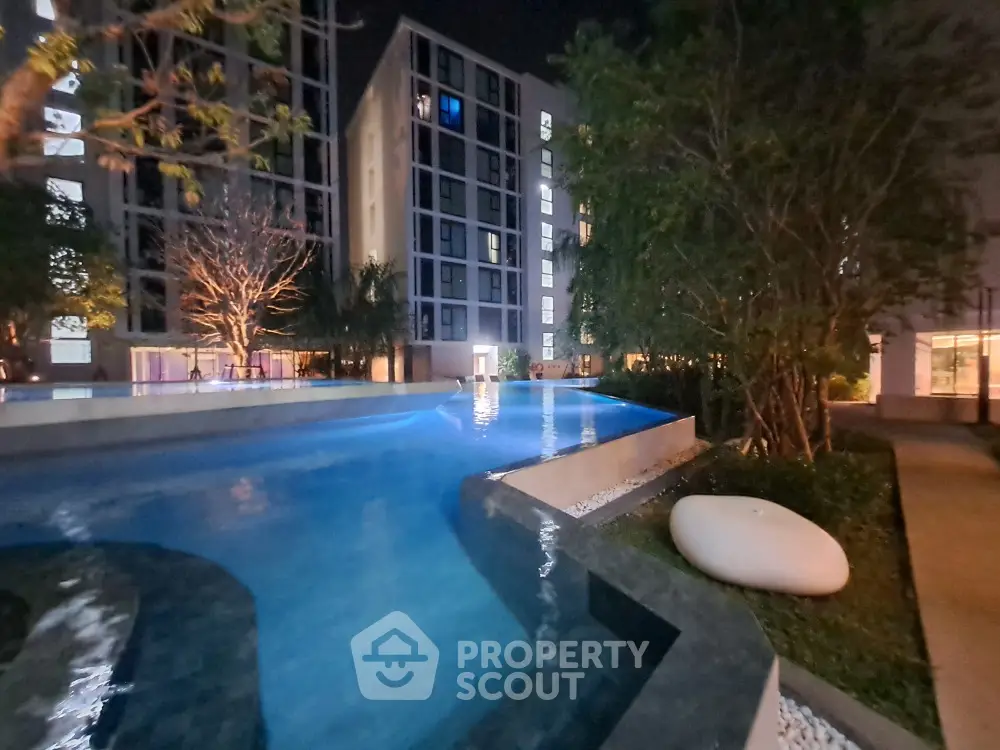 Luxurious night view of modern apartment complex with illuminated swimming pool and lush greenery.