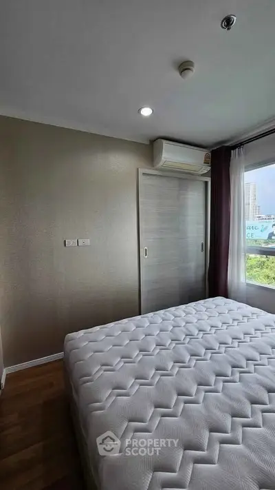 Modern bedroom with large window and city view, featuring a comfortable bed and sleek design.