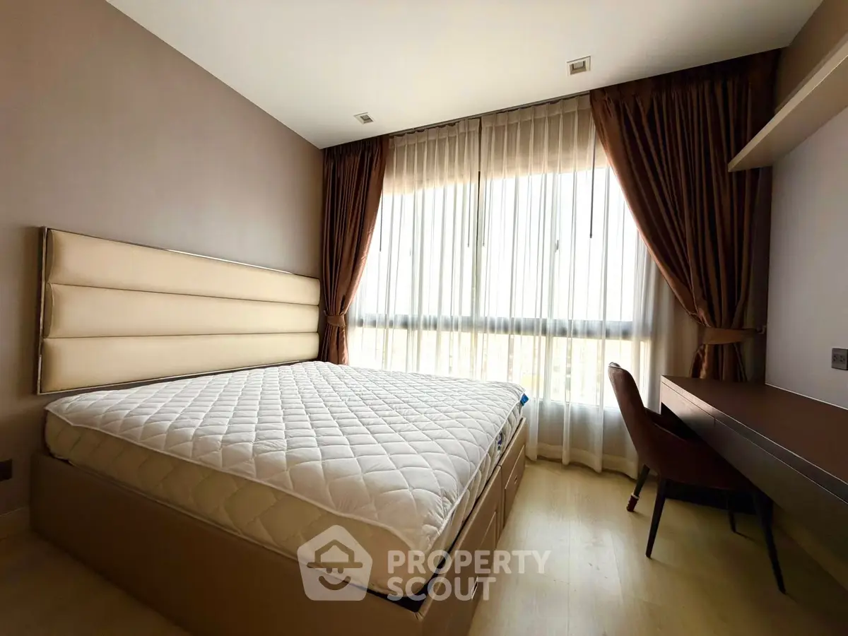 Spacious bedroom with large window and elegant curtains, featuring a comfortable bed and stylish desk.